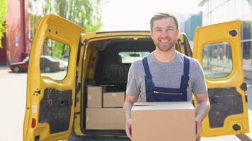 Portrait of a courier holding a parcel, a yellow car in the background. Delivery concept - courier in blue uniform holding package video