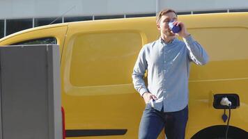 A man drinks coffee while charging an electric car at a charging station. Electric car charging video