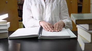 femmina alunno studiando nel un' biblioteca, seduta e lettura un' braille libro video