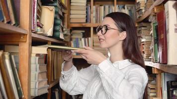 A university student is looking for a book on bookshelves in the library. The student blowing off the dust from the old book video