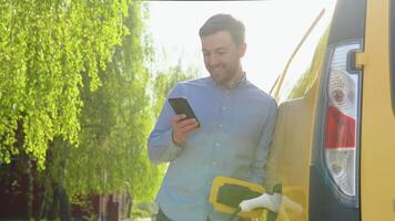 Jeune homme bavarder sur mobile téléphone tandis que électrique voiture est mise en charge sur Extérieur gare. prise de courant mise en charge un électrique voiture de mise en charge station video