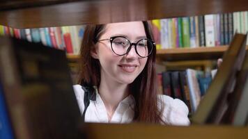 un Universidad estudiante es mirando para un libro en estantería en el biblioteca video