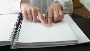 Hand touches the description in Braille. Female student studying in a library, sitting and reading a braille book video