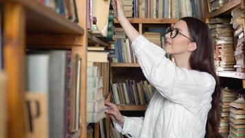 stänga upp attraktiv Tonårs flicka Framställ i bibliotek se på kamera. huvud skott av högre utbildning institution studerande porträtt, excellent studier begrepp video