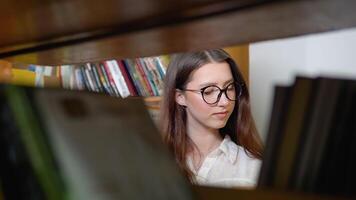 uma pensativo jovem aluna lê uma livro em pé dentro a biblioteca video