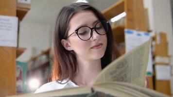 un pensativo joven estudiante lee un libro en pie en el biblioteca video