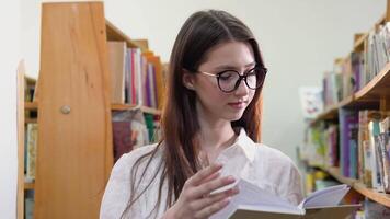 ung flicka i glasögon läser en bok i de universitet bibliotek video