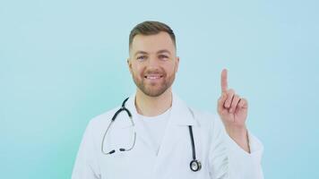 läkare med stetoskop i vit täcka höjer hans index finger upp till ansikte nivå på en blå bakgrund video