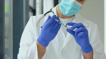 A young doctor in a protective mask draws a vaccine into a syringe video