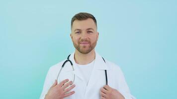 Successful physician in white lab coat looks at the camera and smiles on a blue background video