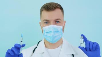 Doctor holds an ampoule with a vaccine and a syringe in his hands on a blue background video