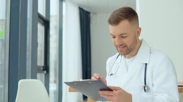 masculino médico escrevendo uma pacientes médico história dentro dele médico escritório video