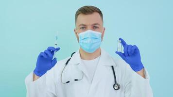 Doctor holds an ampoule with a vaccine and a syringe in his hands on a blue background video