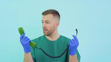 Doctor in a green uniform and blue gloves is surprised to hold an old phone in his hands video