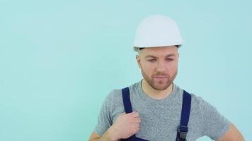 General worker in a helmet and overalls yawns on a blue background video