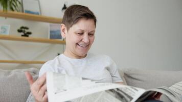 een detailopname visie van een mooi volwassen vrouw is lezing een krant- zittend Aan sofa Bij huis in de ochtend. portret van senior vrouw lezing krant- video