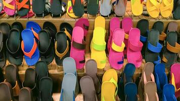 Rows of multicolored rubber sandals and flip flops on wooden shelf display for sale in shopping mall photo