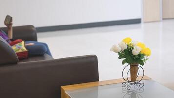 Focus at vintage artificial flowers vase on the table with blurred background of child using smartphone on sofa in living room at home photo