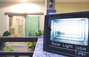 Illuminated LED spotlight solar cell on fence in front of house at night, close up shot with blurred background photo