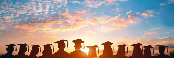 Silhouettes of students wearing graduation caps against the sky at sunset photo