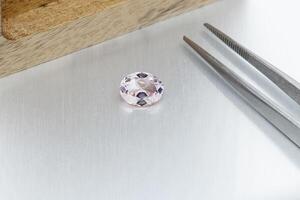 macro mineral faceted stone Morganite with tweezers on a gray background photo