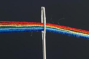 multicolor hilos para de coser en el formar de un arco iris pasar mediante un antiguo aguja en un negro antecedentes foto