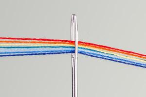 multi-colored threads for sewing in the form of a rainbow pass through an antique needle on a white background photo