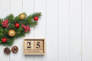 christmas tree branch with toys and gifts and wooden calendar december 25 on wooden background photo