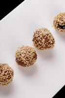 Beautiful candies with sesame seeds on a white plate on a black background photo