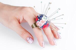 a ring with a small pillow for needles on a hand on a white background photo