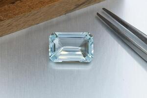 macro mineral faceted stone aquamarine with tweezers on a gray background photo