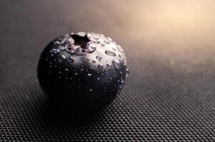 One blueberry covered with water drops on black background. Very detailed macro shoot with copy space photo