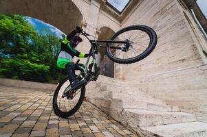 man standing on one wheel of a mountain bike. Horizontal shot outdoors in the city with architecture in the background, wide angle. Guy performs a sports trick photo