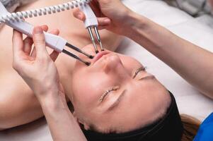 Close-up of a professional cosmetologist's hands touching a woman's cheek with equipment. Young woman lying and relaxing during massage photo