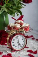 todavía vida en Inglés estilo con escarlata peonías y rojo terciopelo magdalenas con en un plato, té hora en rojo antiguo reloj foto
