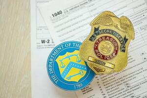 KYIV, UKRAINE - MARCH 9, 2024 US Treasury Police Secret Service Officer badge and Department of Treasury seal on 1040 and W-2 IRS tax forms photo