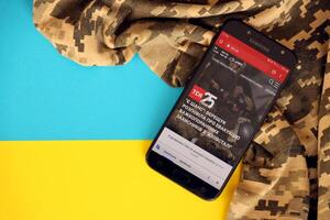 KYIV, UKRAINE - 4 MAY, 2023 TSN ukrainian news portal on smartphone screen with ukrainian flag and camouflage fabric photo