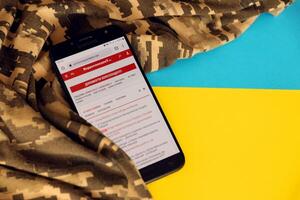 KYIV, UKRAINE - 4 MAY, 2023 Correspondent ukrainian news portal on smartphone screen with ukrainian flag and camouflage fabric photo