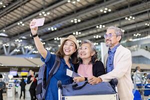 grupo de asiático familia turista pasajeros con mayor es utilizando móvil teléfono a tomar selfie foto a aeropuerto terminal durante vacaciones viaje y largo fin de semana fiesta