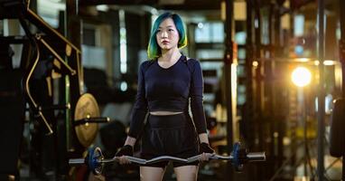 Asian woman is practice weight lifing using easy bar as beginner on barbell for arm and core muscle inside gym with dark background for exercising and workout photo