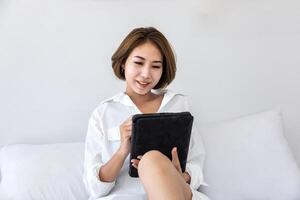 Young pretty girl working from home on her bed using digital tablet to access her business work for education study and online dating service photo