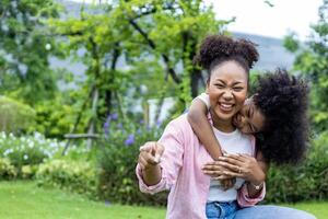 African American mother is playing piggyback riding with her young daughter while having a summer picnic in the public park for wellbeing and happiness photo