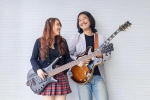 Portrait of Asian family duo rock band of young girl idol on bassist and male on semi hollow electric guitar standing on white background for music, artist, musician concept photo