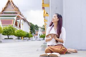 Asian buddhist woman is reading Sanskrit ancient palm leaf manuscript of Tripitaka the Lord Buddha dhamma teaching while sitting in temple on holy full moon day to chant and worship in the monastery photo