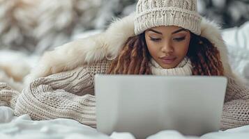 A woman in a white hat sitting in the snow, typing on a laptop photo