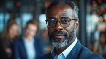 A man with glasses and a beard stands in front of a group of people photo