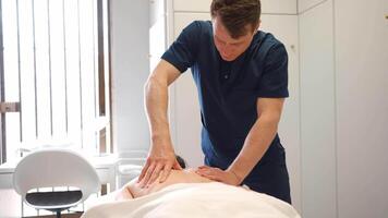 masculino masajeador dando terapéutico y relajante, profundo pañuelo de papel estimulante espalda masaje a un caucásico hembra paciente video