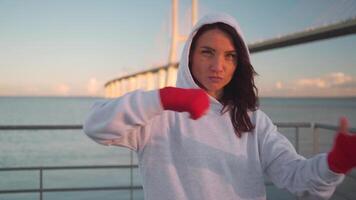 Woman shadow taking fighting pose with her hands wrapped in red boxing tapes with city seascape background. video