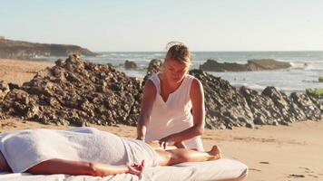 vrouw genieten van professioneel spa hand- massage aan het liegen Aan speciaal tafel Aan strand gedurende vakantie. massage therapeut geven ontspannende massage van de klant armen en schouders video