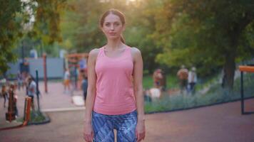 un' donna nel un' rosa serbatoio superiore e blu pantaloni sta nel un' parco video